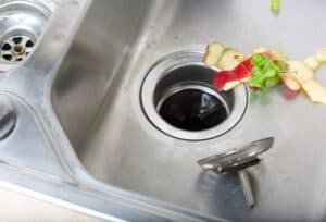 Kitchen sink with food scraps near a residential garbage disposal.