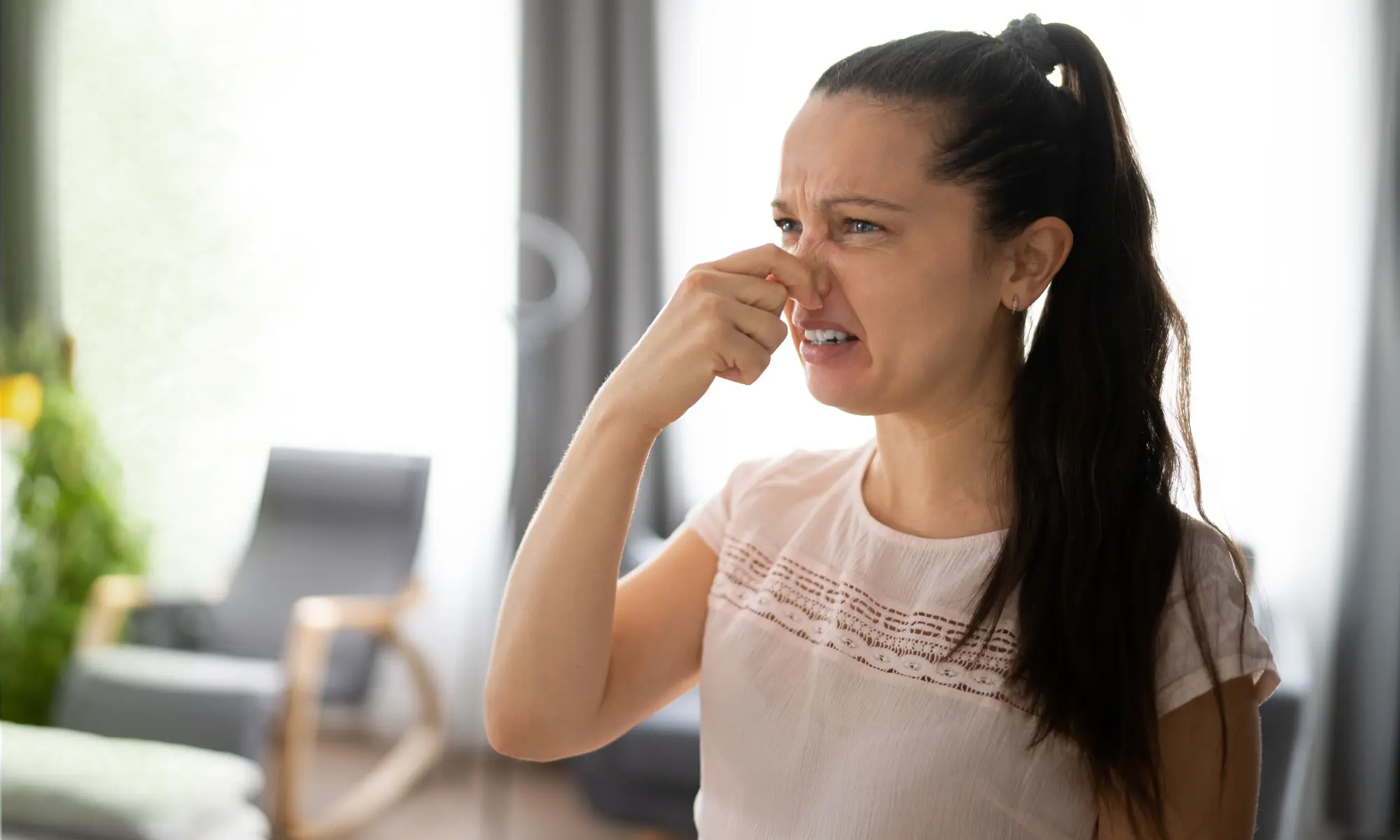 A woman standing indoors reacting to a musty odor.