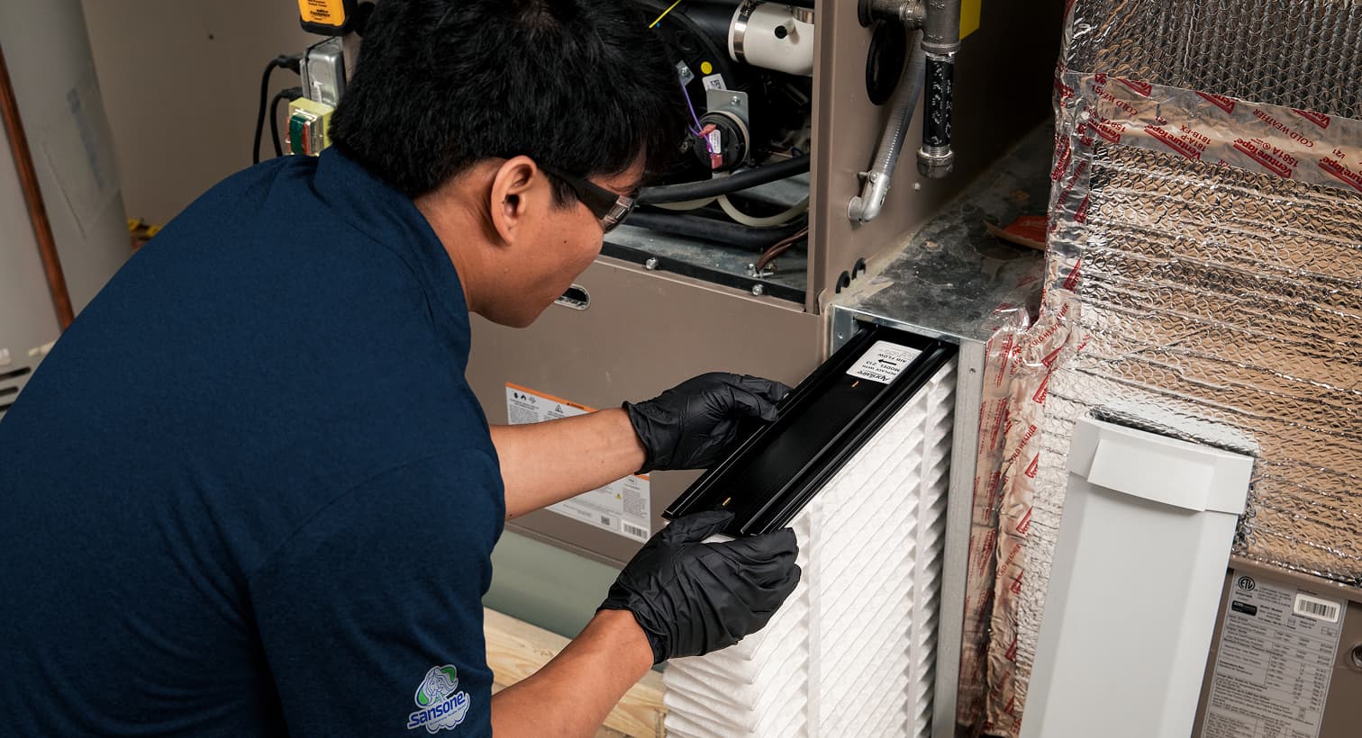 A professional Sansone HVAC technician replacing a clean pleated air filter in an indoor air handler unit during a routine AC maintenance tune-up.