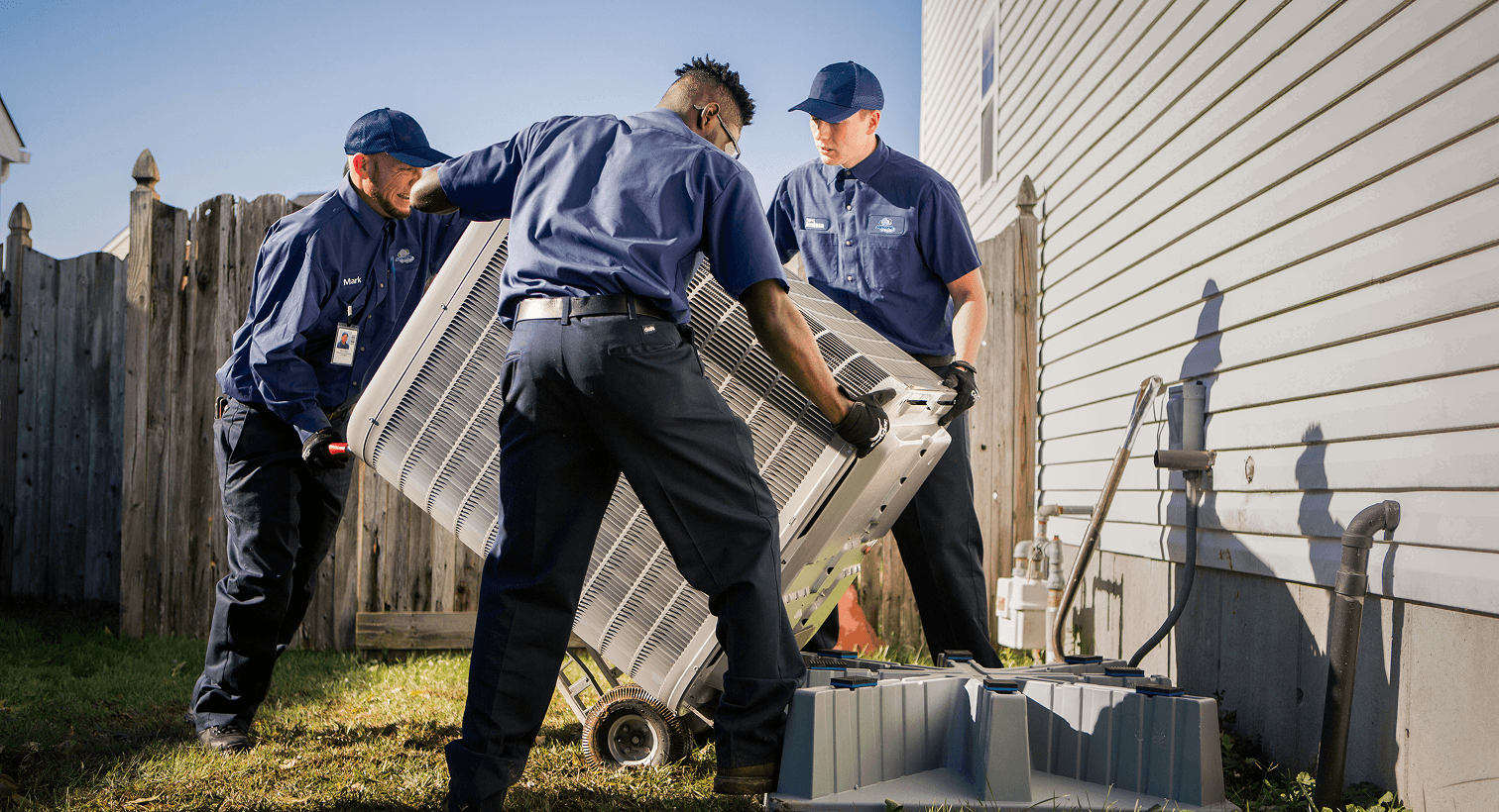 HVAC technicians moving an outdoor air conditioning unit during installation.